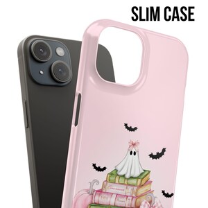 May include: A pink phone case with a ghost sitting on a stack of books. Bats are flying around the ghost. The text "SLIM CASE" is in the upper right corner of the image.