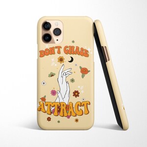 Może przedstawiać: Ż&oacute;łte etui na telefon z kwiatowym wzorem i tekstem "Don't Chase Attract" w retro czcionce. Etui zawiera p&oacute;łksiężyc i dwie dłonie z splecionymi palcami.
