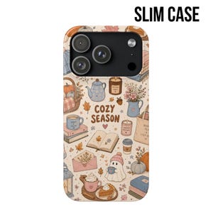 May include: A slim phone case featuring a cream background with a repeating pattern of autumn-themed illustrations including pumpkins, books, candles, a teapot, a ghost, and mugs. The text COZY SEASON is printed in the center in brown letters.