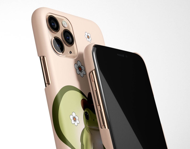 May include: A pink phone case with a green frog wearing a cowboy hat and white flowers. The case is designed for an iPhone with a triple camera lens.