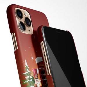 May include: A red iPhone case with a Christmas-themed design featuring a Nutcracker doll, a Christmas tree, and a star. The case has a gold trim and a clear back to show the phone.