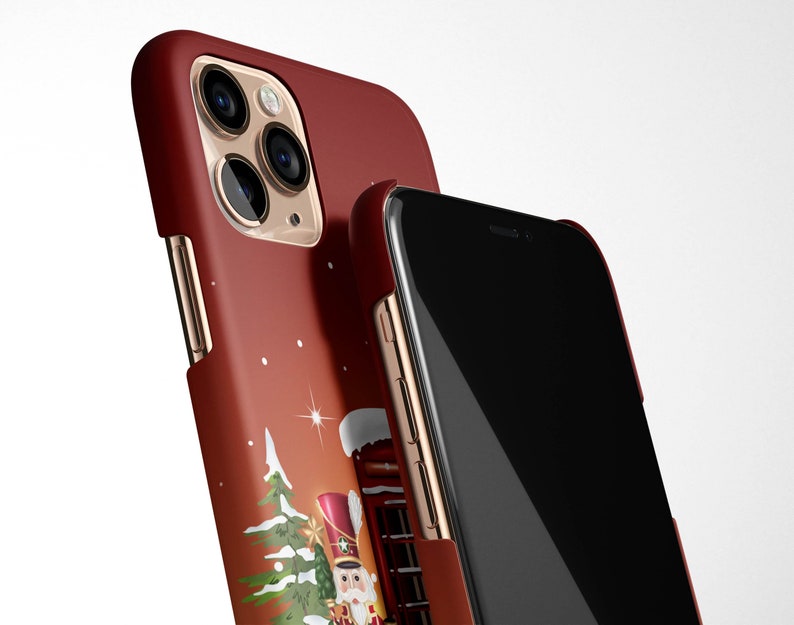 May include: A red iPhone case with a Christmas-themed design featuring a Nutcracker doll, a Christmas tree, and a star. The case has a gold trim and a clear back to show the phone.