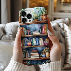 Könnte beinhalten: Eine weiße iPhone-Hülle mit einem Aquarell-Design eines Bücherregals, das mit bunten Büchern und Topfpflanzen gefüllt ist. Die Hülle hat einen Kameraausschnitt und einen blauen Hintergrund.