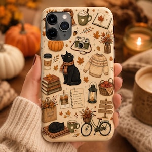 Könnte beinhalten: Eine cremefarbene Handyhülle mit einem herbstlichen Muster aus einer schwarzen Katze mit Schal, einem Fahrrad mit Blumenkorb, einem Bücherstapel, einer Kamera, einem Pullover, einer Laterne, Kürbissen, Ahornblättern und einem Notizblock.