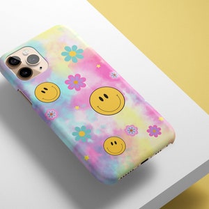 May include: A colorful tie-dye phone case with a pink, blue, and yellow background. The case features a variety of yellow smiley faces and pink and blue flowers.