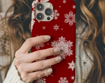 Puede incluir: Funda de teléfono roja con un patrón de copo de nieve blanco. La funda tiene un recorte para el objetivo de la cámara y un borde blanco.