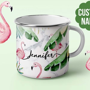 Op de afbeelding: Witte emaille mok met een tropisch ontwerp met roze flamingo's en groene palmbladeren. De mok heeft een zilveren rand en handvat. De naam "Jennifer" staat op de mok.