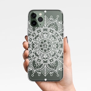 Puede incluir: Una funda transparente para teléfono con un diseño de mandala blanco. La funda tiene un fondo verde y un recorte para la lente de la cámara.