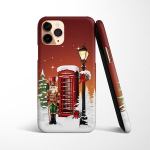 May include: A red phone booth with a nutcracker standing in front of it. The phone booth is decorated with a red bow and green garland. There is a street lamp with a lit light bulb next to the phone booth. The background is a red and white winter scene.