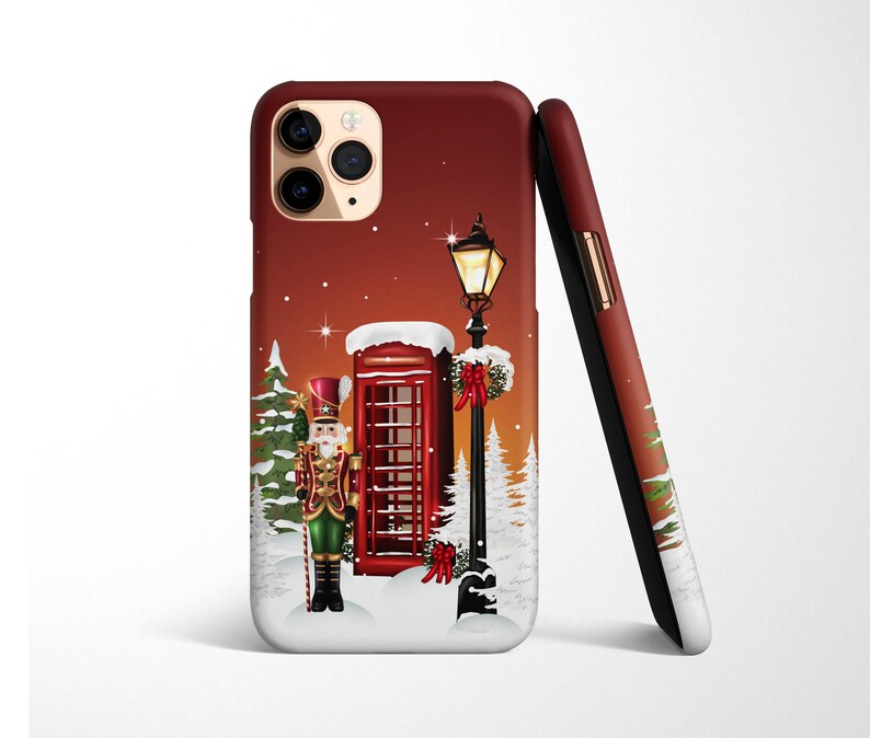 May include: A red phone booth with a nutcracker standing in front of it. The phone booth is decorated with a red bow and green garland. There is a street lamp with a lit light bulb next to the phone booth. The background is a red and white winter scene.