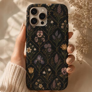 May include: A black smartphone case featuring a repeating gold-lined ogee pattern filled with various botanical illustrations, including pansies, irises, tulips, and small white flowers, creating a detailed floral arrangement across the entire surface.