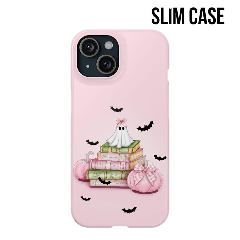 May include: A pink phone case with a ghost sitting on a stack of books and pumpkins. The ghost is white with a pink bow. The books are pink and green with white text. The pumpkins are orange and white. There are black bats flying around the ghost and books.