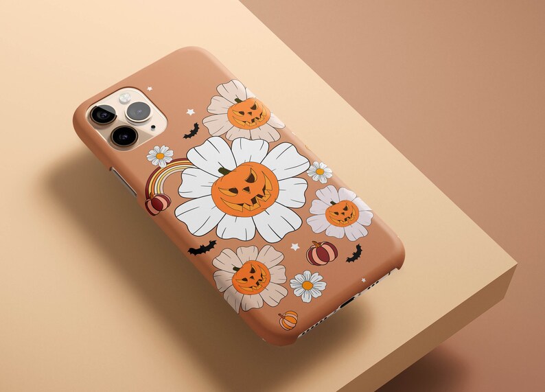 Pu&ograve; includere: Una custodia per iPhone marrone a tema Halloween. La custodia presenta fiori bianchi con zucche arancioni e pipistrelli.
