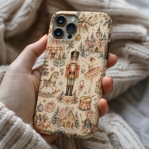 May include: A phone case featuring a detailed, multi-colored illustration of a nutcracker, a ballerina, a rocking horse, a castle, a mouse in a crown, and various holiday-themed gifts and decorations set against a cream-colored background.