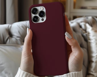May include: A burgundy phone case with a matte finish. The case has a camera cutout with three lenses and a flash. The phone case is held in a person's hands.