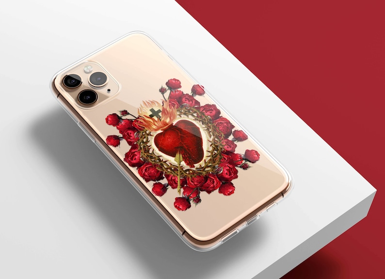 May include: A clear phone case with a gold-colored iPhone inside. The case features a colorful image of a heart with thorns and a cross, surrounded by red roses.