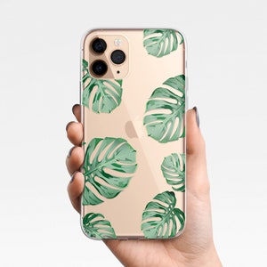 May include: A clear phone case with a gold background and a pattern of green tropical leaves. The case has a cutout for the camera lens.