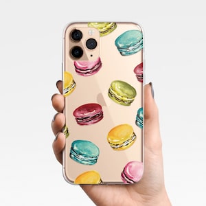 May include: A clear phone case with a pattern of colorful macarons on a gold background. The case has a camera cutout and a cutout for the phone's buttons.