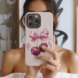 Op de afbeelding: Lichtroze telefoonhoesje met een aquarel illustratie van twee kersen, een roze strik en druipend sap. De hoes heeft een glanzende afwerking en is ontworpen voor een smartphone.