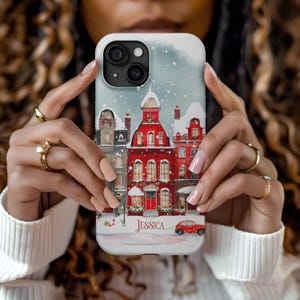 May include: A white phone case with a winter scene featuring red brick buildings, snow, and a red car. The name "Jessica" is printed on the case.