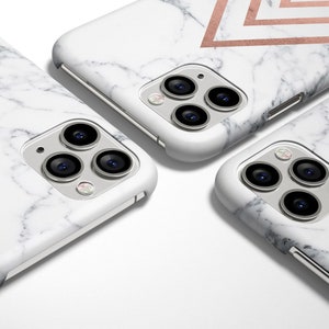 K&ouml;nnte beinhalten: Drei wei&szlig;e iPhone-H&uuml;llen mit Marmormuster und geometrischen Designs in Ros&eacute;gold. Die H&uuml;llen haben eine erh&ouml;hte Kamerabuckel mit drei Objektiven.