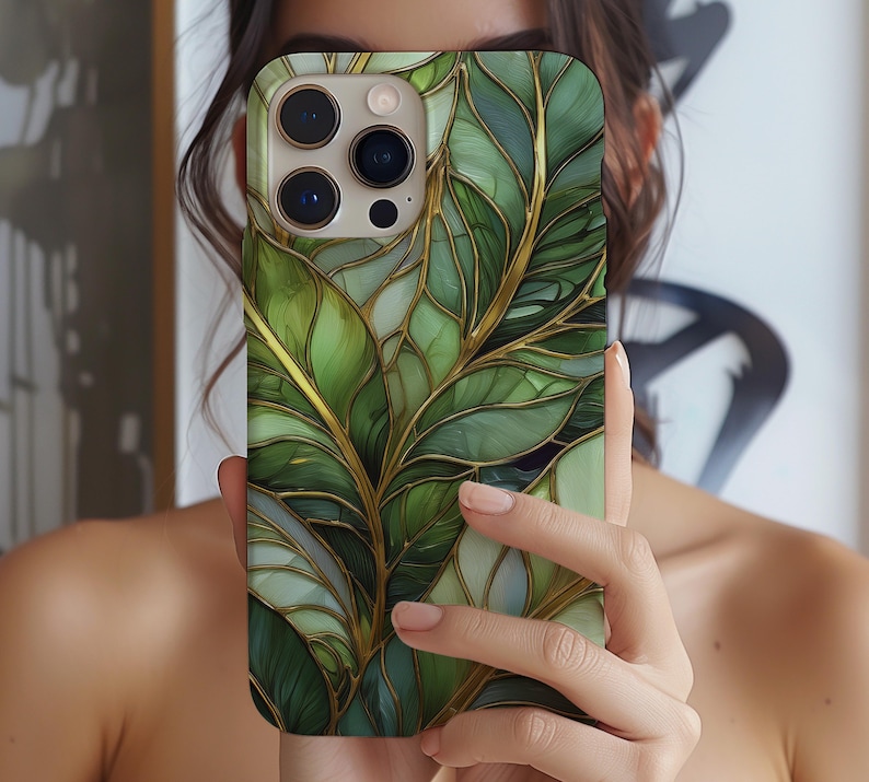 May include: A phone case featuring a green and gold leaf design. The case has a glossy finish and a detailed pattern of leaves with gold accents. The phone case is held in a person's hand.