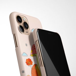 May include: A pink phone case with a mushroom and snail design. The case has a gold trim and a black phone screen.