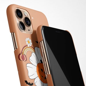 Pu&ograve; includere: Una custodia per telefono marrone con un design a tema Halloween che presenta una zucca, un arcobaleno e una margherita. La custodia &egrave; mostrata sopra un telefono nero.