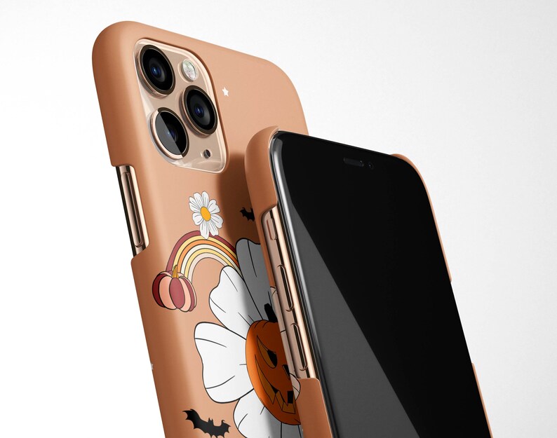 Pu&ograve; includere: Una custodia per telefono marrone con un design a tema Halloween che presenta una zucca, un arcobaleno e una margherita. La custodia &egrave; mostrata sopra un telefono nero.