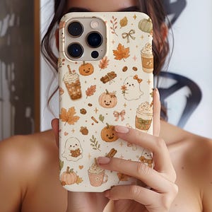 May include: A cream-coloured smartphone case featuring a repeating pattern of autumn-themed illustrations including orange pumpkins, brown maple leaves, white ghosts, cinnamon sticks, acorns, bows, and cups of coffee with whipped cream toppings.
