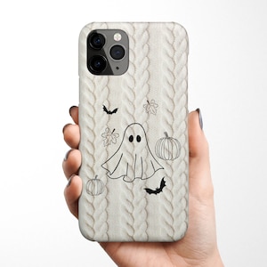 May include: A white iPhone case with a knitted pattern and Halloween-themed illustrations. The illustrations include a ghost, pumpkins, bats, and leaves.