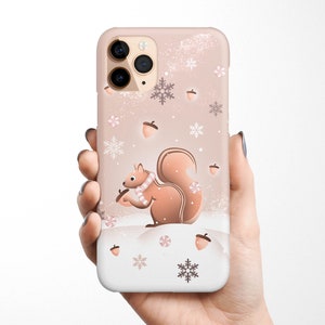 May include: A pink iPhone case with a wintery design featuring a squirrel, snowflakes, and acorns.