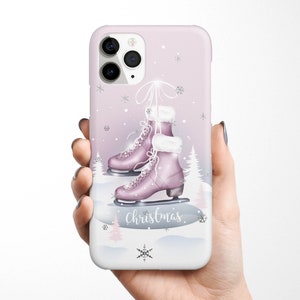 May include: A pink iPhone case with a winter scene featuring a pair of pink ice skates, snowflakes, and the word "Christmas".