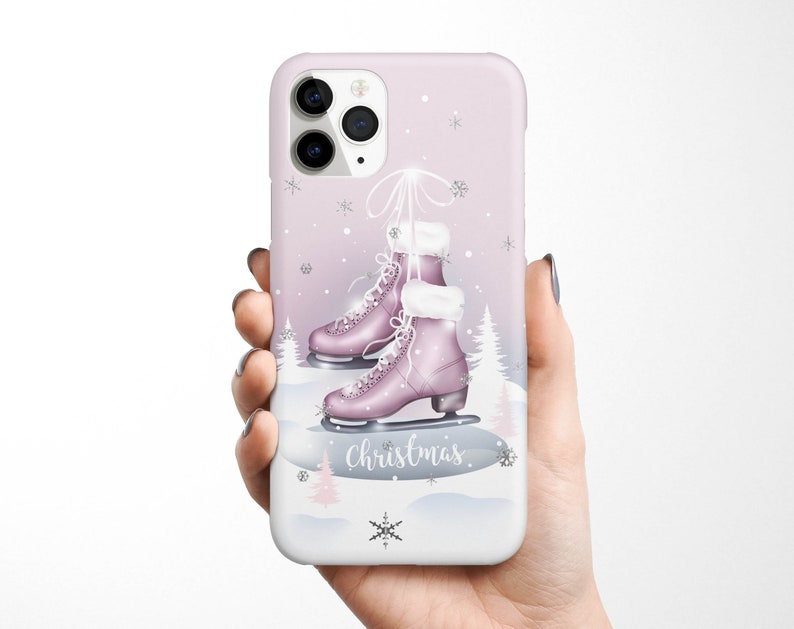 May include: A pink iPhone case with a winter scene featuring a pair of pink ice skates, snowflakes, and the word "Christmas".