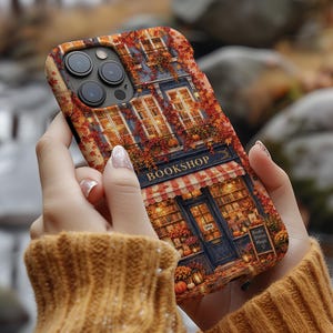 May include: A phone case featuring a detailed illustration of a bookstore exterior during autumn, with orange and red foliage, a striped awning, and a sign that reads BOOKSHOP and Books Stories Magic. The design includes warm lighting and pumpkins.