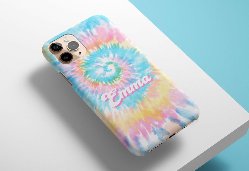 May include: A smartphone case with a colorful tie-dye pattern in shades of blue, pink, yellow, and white. The name "Emma" is printed in a pink script font across the case. The case is on a white surface.