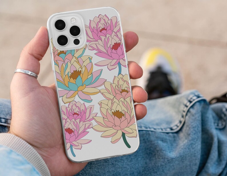 May include: A white iPhone case with a floral design featuring pink, yellow, and blue water lilies. The case has a clear back and a white border.