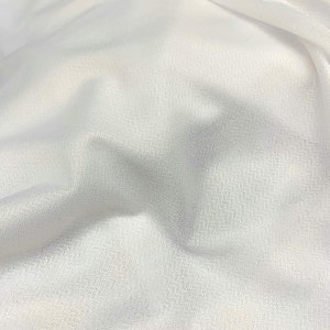 May include: White sheer fabric with a smooth, slightly textured surface. The fabric is draped and folded, showing its soft and flowing nature.
