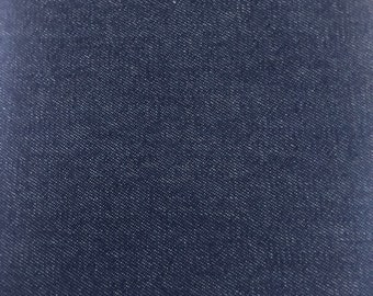 May include: Close-up of a swatch of dark blue denim fabric. The fabric has a textured surface with a diagonal weave pattern. The color is a deep indigo, with subtle variations in tone.