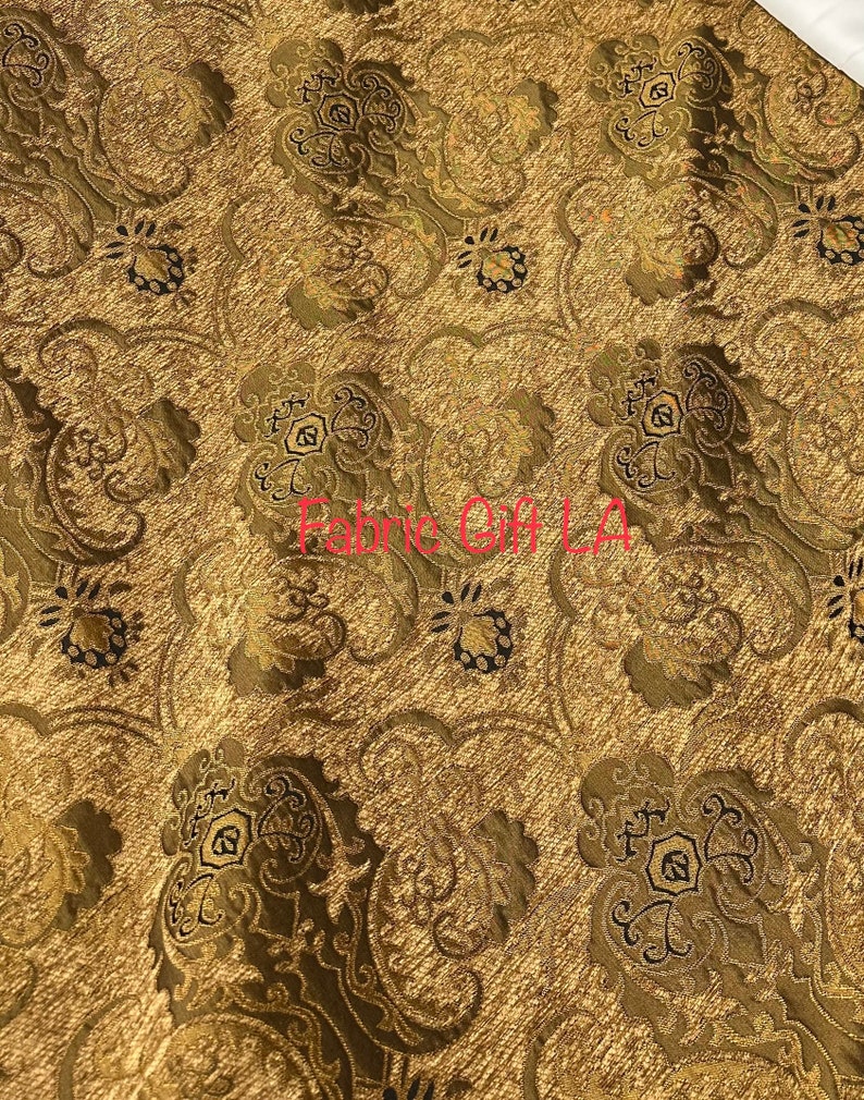 May include: Gold fabric with a black and brown damask pattern. The fabric has a subtle sheen and a textured surface.