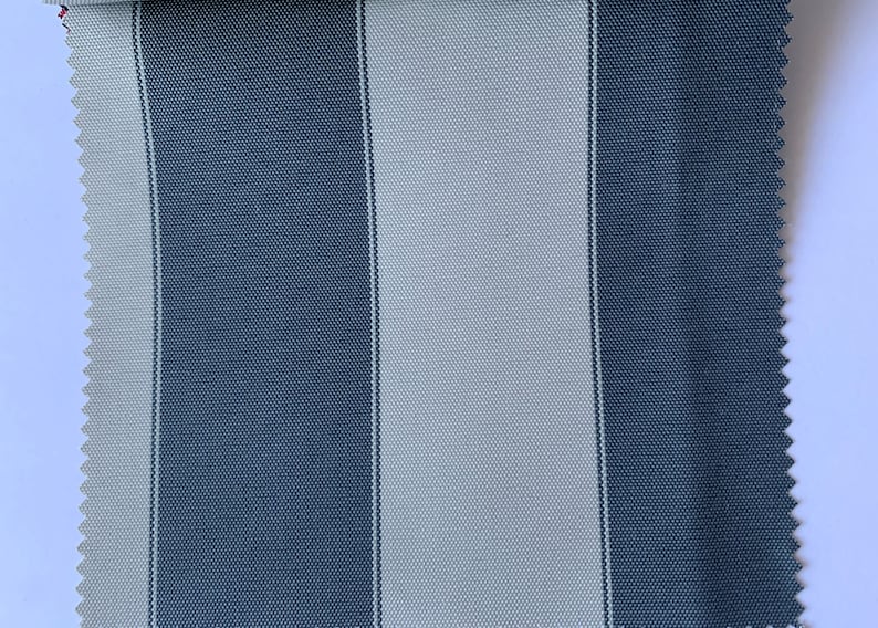May include: A fabric swatch featuring a vertical striped pattern in shades of blue and light gray. The fabric has a textured appearance and a serged edge on one side. The stripes are of equal width.