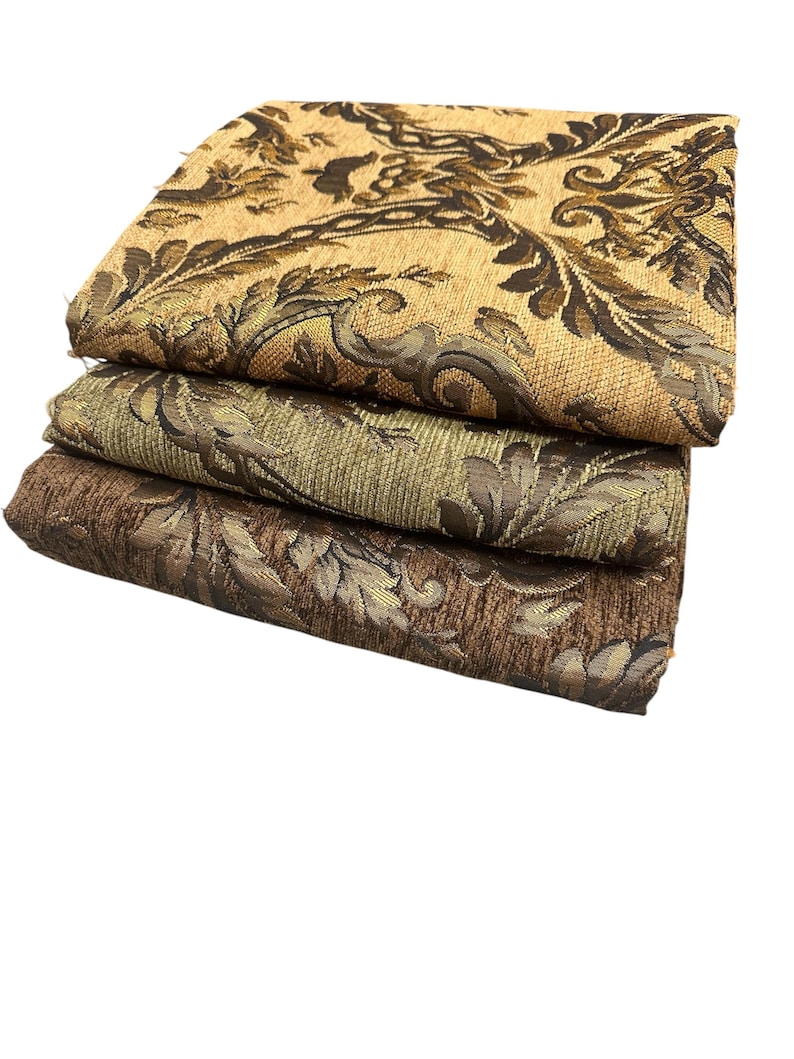 Puede incluir: Tres piezas de tela dobladas con un estampado de damasco floral. La pieza superior es de color beige y marr&oacute;n, la pieza central es de color verde oliva y marr&oacute;n, y la pieza inferior es de color marr&oacute;n y dorado. La tela tiene un aspecto texturizado.