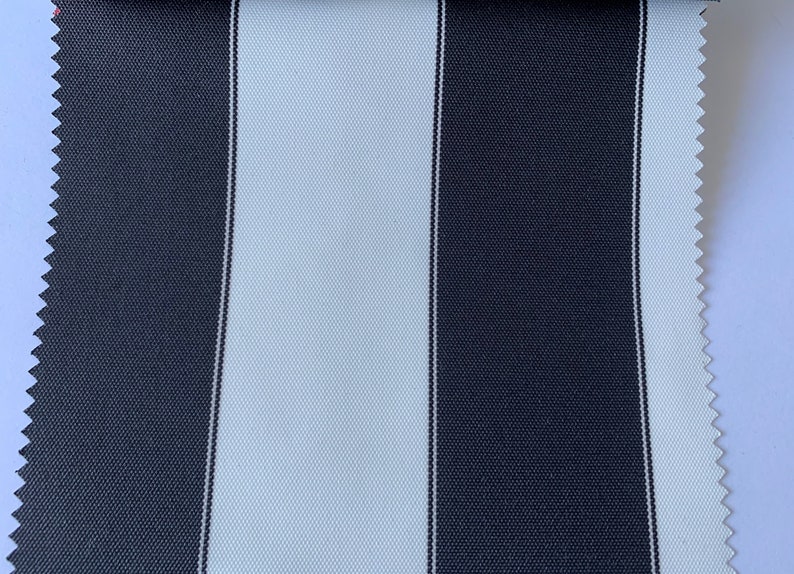 May include: Close-up of a fabric sample with a bold striped pattern. Alternating vertical stripes in navy blue and white create a classic design. The fabric has a textured appearance, and the edge is cut with a zig-zag pattern. Ideal for upholstery or outdoor use.