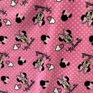 May include: Pink fabric with a white polka dot pattern featuring repeated images of Minnie Mouse with the text "Minnie" printed on the fabric.
