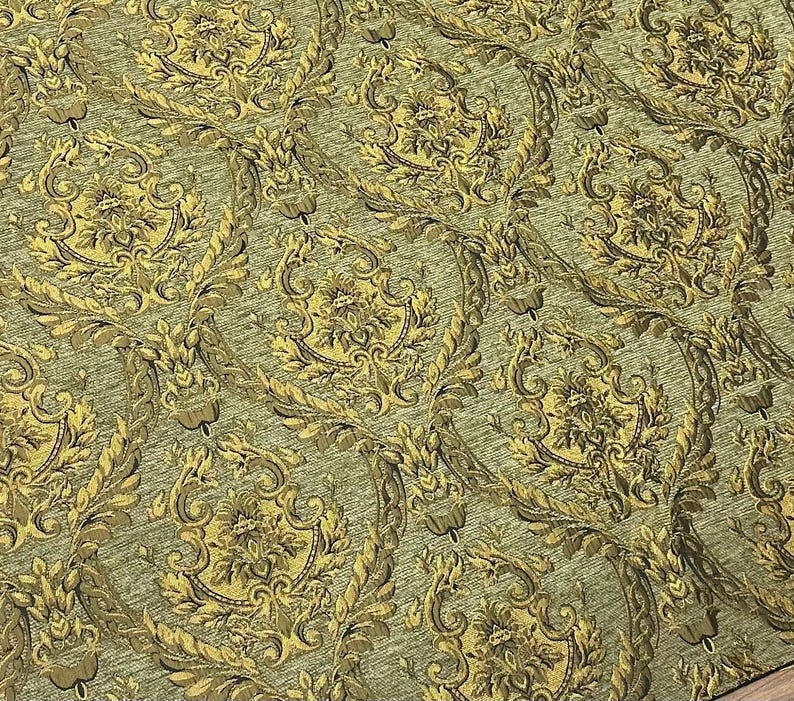 Puede incluir: Primer plano de una tela estampada con un dise&ntilde;o repetitivo. El patr&oacute;n presenta motivos florales y de hojas ornamentados y estilizados en tonos dorados y marrones sobre un fondo verde apagado. La tela tiene una apariencia texturizada.