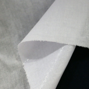 Puede incluir: Una pieza de tela blanca con una textura ligera y transparente y un tejido visible. El material está doblado para revelar una parte inferior lisa y ligeramente reflectante, mostrando el contraste entre la parte superior mate y el brillo sutil.