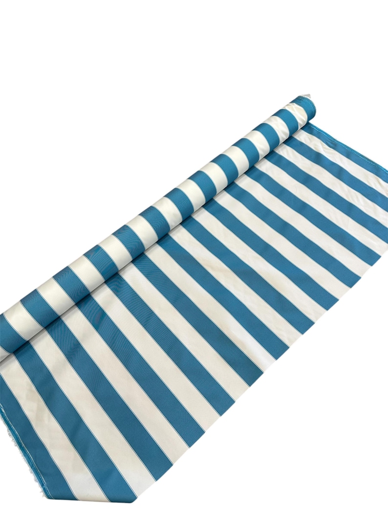 May include: A roll of fabric with alternating white and teal blue stripes. The fabric is partially unrolled, revealing the pattern. The stripes are evenly spaced and run diagonally across the fabric. The background is plain white.