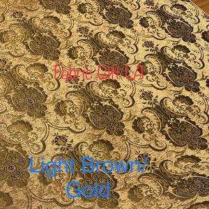 May include: Close-up of a fabric with a light brown and gold paisley pattern. The fabric is textured and has a subtle sheen. The text "Fabric Gift LA" is visible in the image.