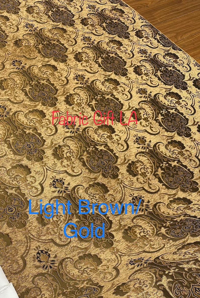 May include: Close-up of a fabric with a light brown and gold paisley pattern. The fabric is textured and has a subtle sheen. The text "Fabric Gift LA" is visible in the image.