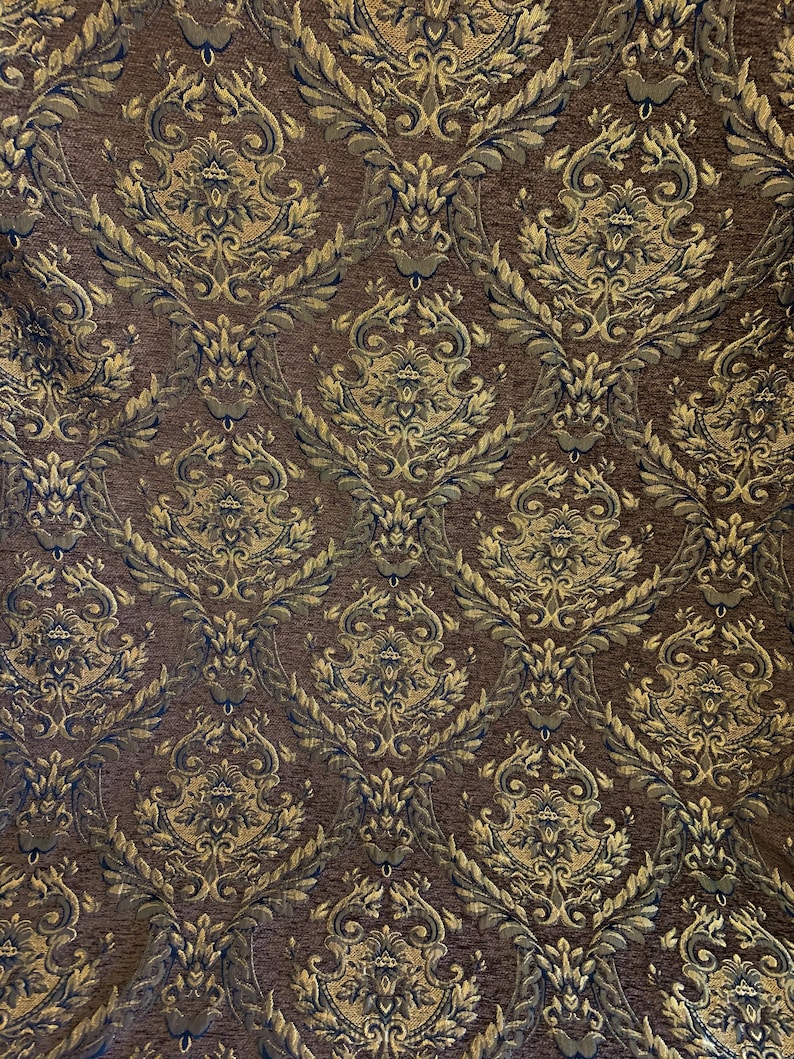 Puede incluir: Primer plano de una tela marr&oacute;n con un estampado damasco dorado y azul marino. El dise&ntilde;o ornamentado presenta hojas y motivos florales en espiral, creando una apariencia lujosa y texturizada. La tela es adecuada para tapicer&iacute;a o cortinas.